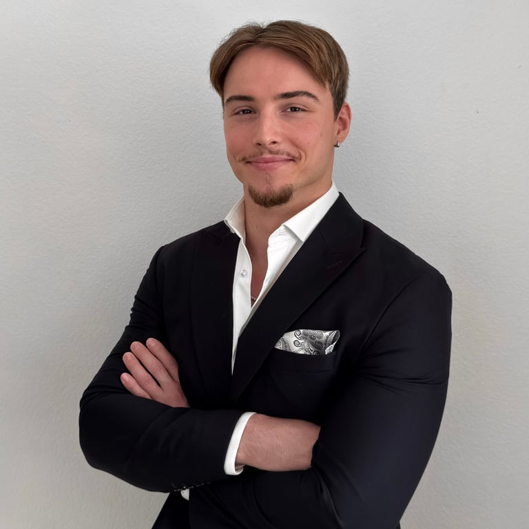 Professional headshot of a man in a black blazer with white dress shirt, arms crossed, smiling at camera against white background
